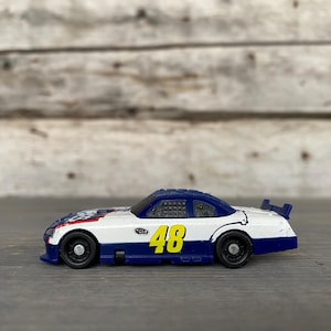 May include: A white, blue, and yellow toy race car with the number 48 on the side. The car has black wheels and a spoiler. The car is a miniature replica of a stock car.