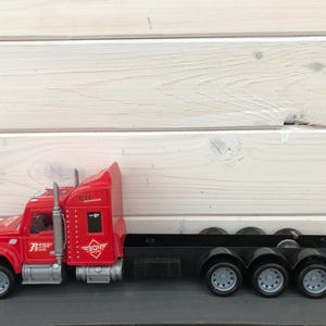 May include: A red toy semi-truck with a black trailer. The truck has silver accents and the words "Power Truck" and "BONE" are visible. The trailer has six wheels.