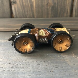 May include: A vintage toy car with a brown and blue body, black tires, and gold-colored wheel details. The toy car is a miniature replica of a race car.