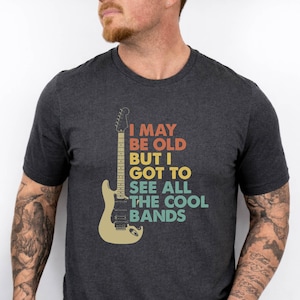 May include: A white ceramic mug with a black handle and the text "But First, Coffee" in a black, bold font. The mug is sitting on a wooden surface. The mug is approximately 4 inches tall.