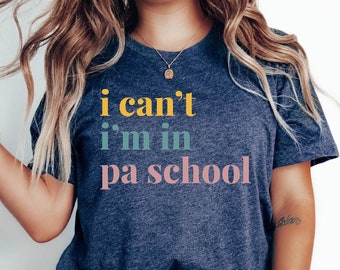 Puede incluir: Una camiseta azul marino con el texto "i can't i'm in pa school" en letras de colores.