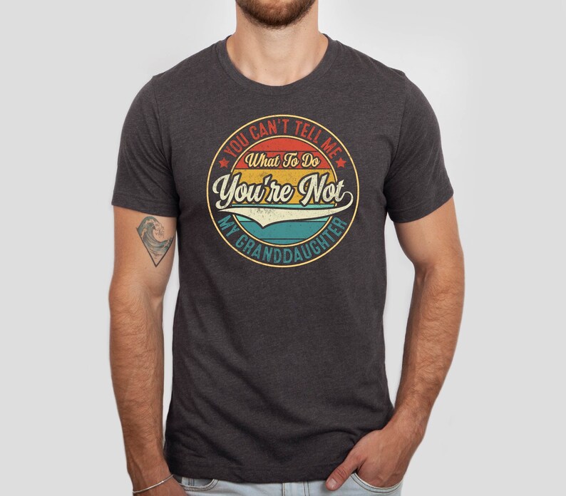 May include: A dark heather grey t-shirt with a vintage-style graphic that says "You Can't Tell Me What To Do You're Not My Granddaughter".