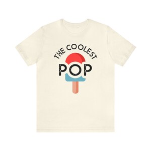Puede incluir: Camiseta de color crema con el texto "THE COOLEST POP" sobre un gr&aacute;fico de paleta. El dise&ntilde;o de la paleta incluye colores rojo, azul y marr&oacute;n. La camiseta est&aacute; hecha de un material suave.