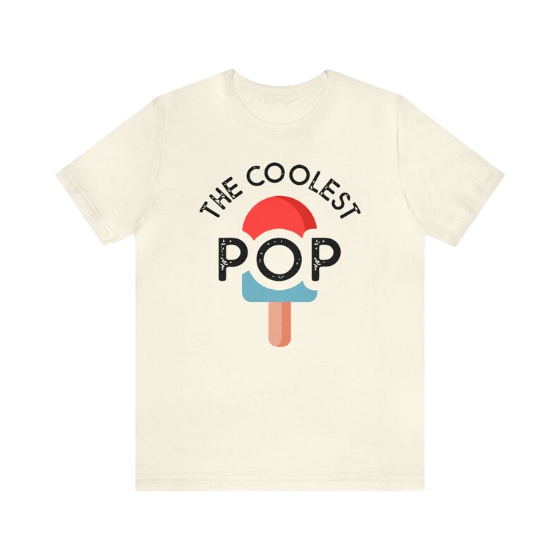 Puede incluir: Camiseta de color crema con el texto "THE COOLEST POP" sobre un gr&aacute;fico de paleta. El dise&ntilde;o de la paleta incluye colores rojo, azul y marr&oacute;n. La camiseta est&aacute; hecha de un material suave.