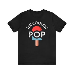 Puede incluir: Camiseta negra con el texto "THE COOLEST POP" sobre un gr&aacute;fico de paleta. La paleta tiene una parte superior roja, un centro azul y un palo marr&oacute;n. El texto y el gr&aacute;fico son blancos.