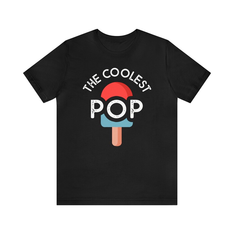 Puede incluir: Camiseta negra con el texto "THE COOLEST POP" sobre un gr&aacute;fico de paleta. La paleta tiene una parte superior roja, un centro azul y un palo marr&oacute;n. El texto y el gr&aacute;fico son blancos.