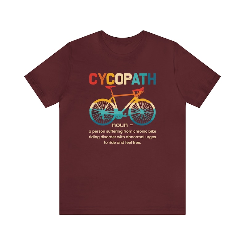 May include: A maroon t-shirt with a vintage-style graphic of a bicycle and the text "CYCOPATH" with a definition: "a person suffering from chronic bike riding disorder with abnormal urges to ride and feel free."