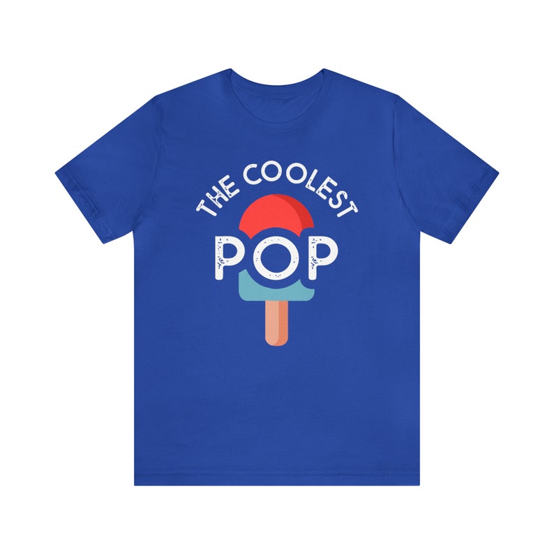 Puede incluir: Camiseta azul real con el texto "THE COOLEST POP" sobre un gr&aacute;fico de paleta. La paleta tiene una parte superior roja, un medio azul claro y un palo marr&oacute;n. El texto y el gr&aacute;fico son blancos.