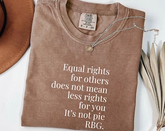 May include: A brown Comfort Colors t-shirt with the text "Equal rights for others does not mean less rights for you. It's not pie. RBG." A silver necklace with a pendant is on the shirt.