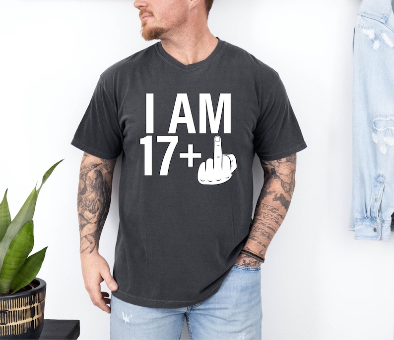 May include: A black t-shirt with white text that reads 'I AM 17+' with a middle finger emoji next to the plus sign.