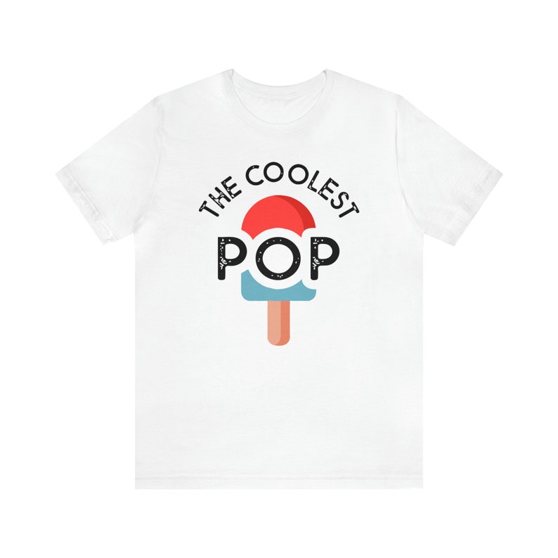 Puede incluir: Camiseta blanca con el texto "THE COOLEST POP" sobre un gr&aacute;fico de paleta. La paleta tiene una parte superior roja, un centro azul y un palo marr&oacute;n. El texto y el gr&aacute;fico son negros.