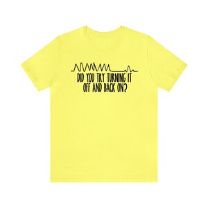 May include: A yellow t-shirt with black text that reads "DID YOU TRY TURNING IT OFF AND BACK ON?" above a line graph design. The shirt is a solid, bright yellow color.