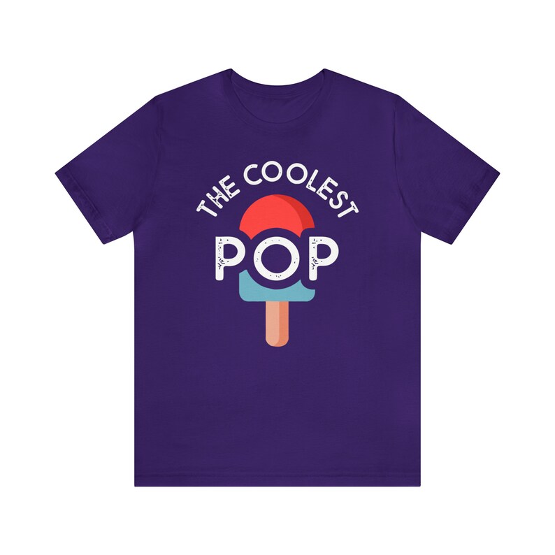 Puede incluir: Una camiseta morada con las palabras "THE COOLEST POP" en blanco sobre un gr&aacute;fico de paleta. La paleta tiene una parte superior roja, un centro azul y un palo marr&oacute;n. La camiseta est&aacute; hecha de un material suave.