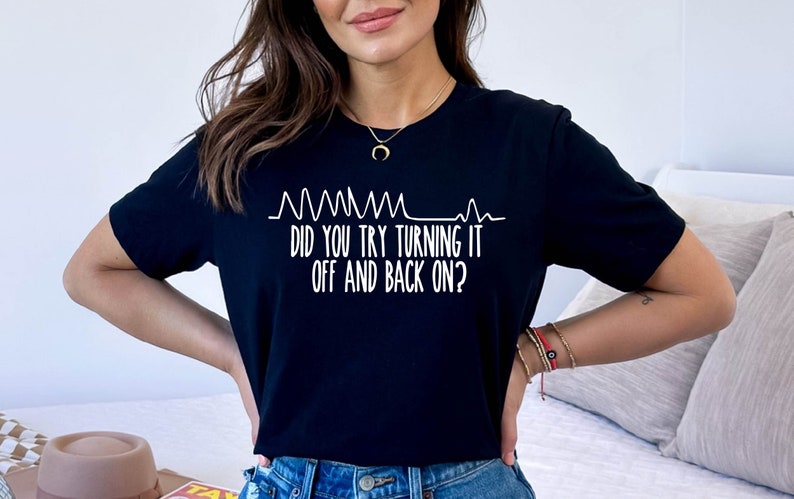 May include: Black t-shirt with white text and a graphic resembling a heartbeat monitor. The text reads, "DID YOU TRY TURNING IT OFF AND BACK ON?" A casual, everyday tee.