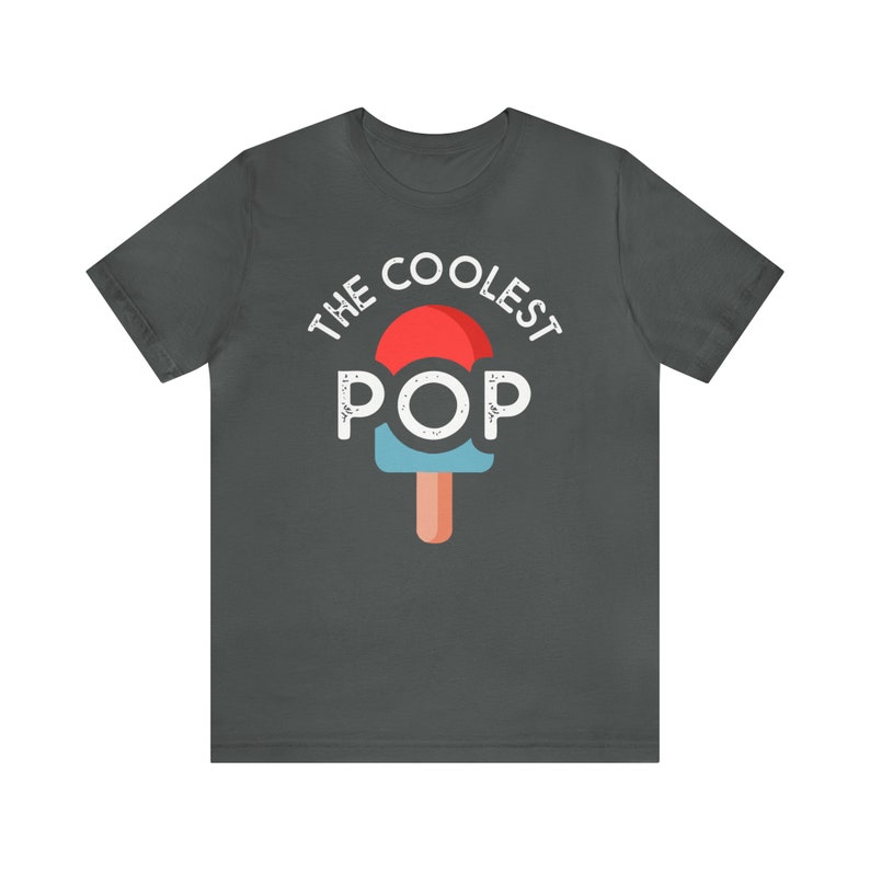 Puede incluir: Camiseta gris oscuro con el texto "THE COOLEST POP" sobre un gr&aacute;fico de paleta de helado roja, azul y naranja. La camiseta es de cuello redondo y manga corta.
