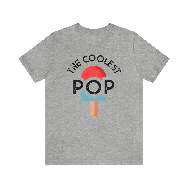 Puede incluir: Camiseta gris jaspeado con la frase "THE COOLEST POP" sobre un gr&aacute;fico de paleta helada. La paleta tiene la parte superior roja, el centro azul y un palo naranja claro. La camiseta es de cuello redondo y manga corta.