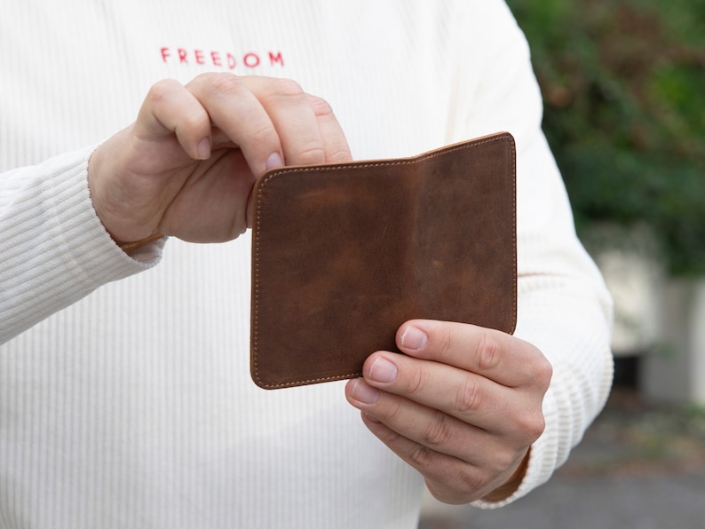 May include: A brown leather wallet with a stitched edge. The wallet is open and the inside is visible.