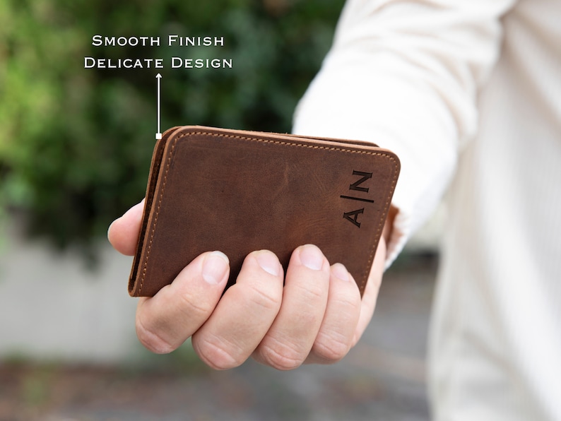 May include: A brown leather wallet with the initials "A|N" embossed on the front. The wallet has a smooth finish and a delicate design.