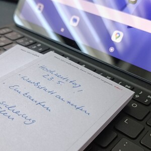May include: A white notepad with blue handwritten text on it. The text says "Hochzeitstag! 23.5. Werkstatt anrufen. Ein kaufen. Versicherung pr&uuml;fen."