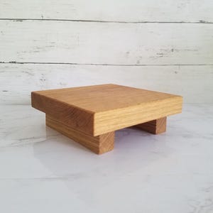 Könnte beinhalten: Ein kleiner, rechteckiger Holzaufsteller mit natürlichem Finish. Der Aufsteller besteht aus massivem Holz und hat eine flache Oberseite, die von vier kurzen Beinen getragen wird. Die Holzmaserung ist sichtbar und verleiht ihm einen rustikalen Charme.