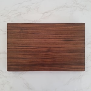 May include: A rectangular wooden cutting board made of dark brown walnut wood.
