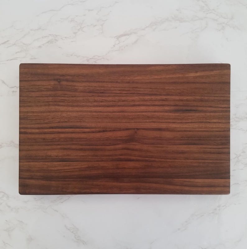 May include: A rectangular wooden cutting board made of dark brown walnut wood.
