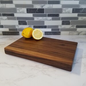 May include: A large, rectangular, dark brown wooden cutting board with a smooth surface. Two lemons, one whole and one sliced in half, are placed on the board.