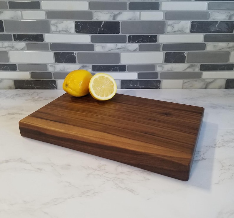 May include: A large, rectangular, dark brown wooden cutting board with a smooth surface. Two lemons, one whole and one sliced in half, are placed on the board.