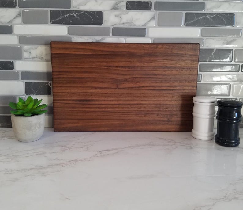 May include: A large, rectangular, brown wooden cutting board with a wood grain pattern. The cutting board is sitting on a white countertop.