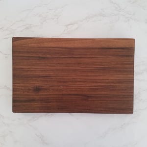May include: A rectangular wooden cutting board with a dark brown wood grain finish.
