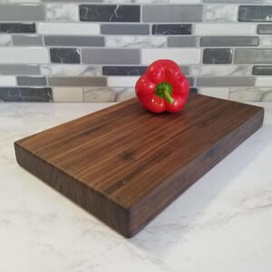 May include: A large, rectangular, dark brown wooden cutting board with a red bell pepper on top.