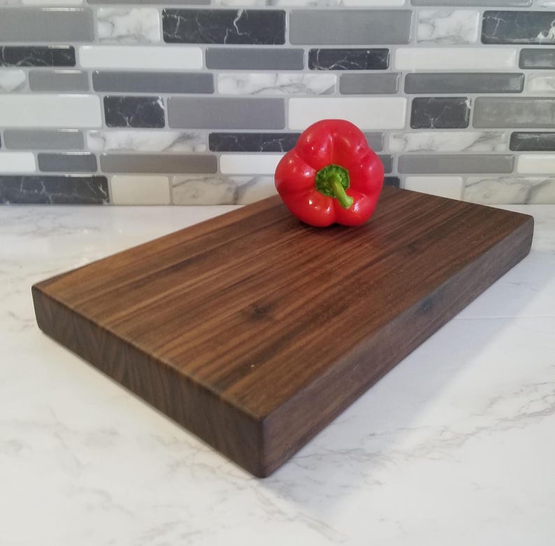 May include: A large, rectangular, dark brown wooden cutting board with a red bell pepper on top.