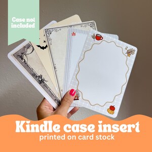 May include: A hand holds a stack of Kindle case inserts printed on card stock. The inserts feature various designs, including a gun, a bat, and a fall-themed border with a coffee cup and pumpkins. Text on the image reads "Case not included."