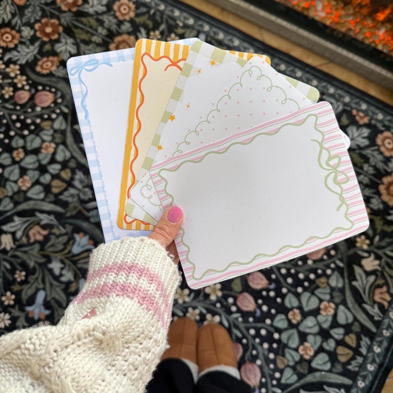 May include: A hand holds a stack of decorative paper sheets with various pastel borders. The sheets feature designs like gingham, scalloped edges, and bows. The color palette includes blue, yellow, green, and pink, creating a whimsical aesthetic.