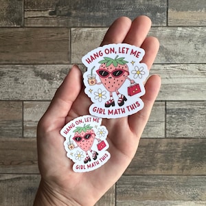 May include: Two stickers featuring a cartoon strawberry wearing sunglasses and holding a shopping bag and a cup of coffee. The text on the stickers reads "Hang on, let me girl math this".
