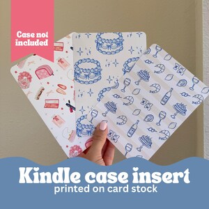 May include: Three different designs of printed card stock inserts for a Kindle case. The designs feature blue and white patterns with illustrations of cakes, wine glasses, lemons, and shrimp. The text "Kindle case insert printed on card stock" is at the bottom of the image.