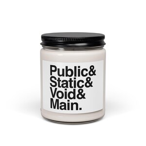May include: A cylindrical glass candle jar with a black metal lid, filled with off-white wax. A white rectangular label on the front features the black text: Public& Static& Void& Main. The container has a smooth, clear glass finish.