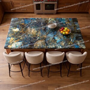 Puede incluir: Isla de cocina con encimera de piedra azul, dorada y marrón. Cuatro taburetes de bar tapizados en beige con patas de metal negro rodean la isla. Una olla de acero inoxidable y un frutero están sobre la encimera. El texto "www.etsy.shop/zayaanfoundrycraft.com" es visible.