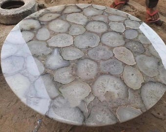May include: A round table top made of white agate slices. The slices are arranged in a circular pattern and have a natural, organic look. The table top is polished and has a glossy finish.