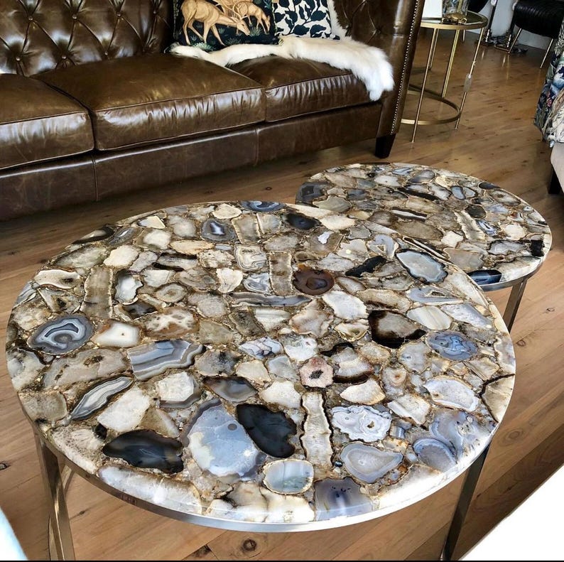 May include: Two round agate coffee tables with a silver metal base. The tabletops are made of natural agate slices in shades of brown, gray, and white.