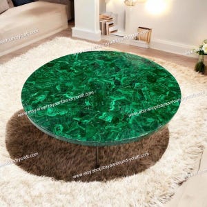 May include: A round green malachite coffee table with a polished surface. The table has a single metal leg and is sitting on a white fluffy rug.