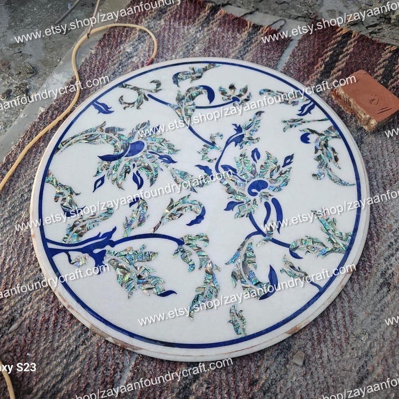 May include: Round white marble table top with a blue and green floral design inlaid with mother of pearl. The design features intricate floral patterns with blue outlines and green and blue mother of pearl accents.