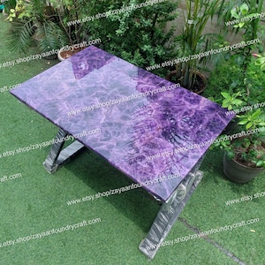 Könnte beinhalten: Ein lila-grauer Harztisch mit einem einzigartigen Marmormuster. Der Tisch hat ein schlichtes, modernes Design mit einem X-förmigen Gestell.