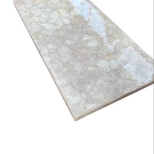 Puede incluir: Azulejo decorativo rectangular gris claro con acabado brillante. La superficie del azulejo presenta un patrón de mosaico, con formas irregulares y sutiles variaciones de tono. Los bordes son limpios y definidos, creando una estética moderna.