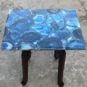 May include: A small blue agate table with a dark wood base. The table top is made of polished agate with a blue and white pattern.