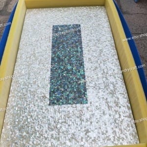 May include: A rectangular mosaic tile with a mother-of-pearl finish and a central rectangular section of iridescent tiles. The tile is set within a yellow and blue frame. The text "www.etsy.shop/zayaanfoundrycraft.com" is visible.