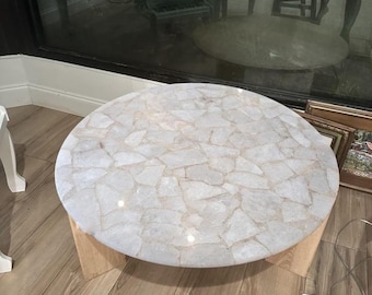Puede incluir: Mesa de centro redonda con tapa blanca estilo mosaico. La tapa está hecha de piezas de forma irregular, creando un patrón único. La base es de madera clara, proporcionando un contraste natural.