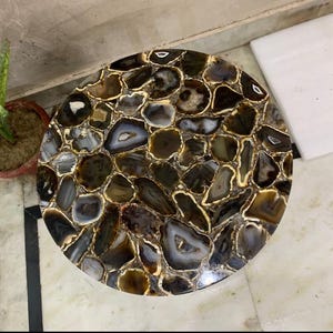 Puede incluir: Mesa redonda de ágata con un patrón marrón y blanco. La mesa está hecha de muchas piezas pequeñas de ágata que han sido cortadas y pulidas.