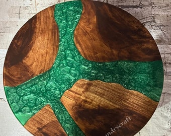 May include: Round wooden table top with a green epoxy resin design. The resin has a swirling pattern and is embedded in the wood. The table top is approximately 46 cm in diameter.