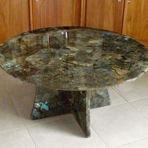 Puede incluir: Una mesa de centro redonda con una tapa única de piedra verde y azul multicolor. La mesa tiene una base de cuatro patas hecha de la misma piedra.